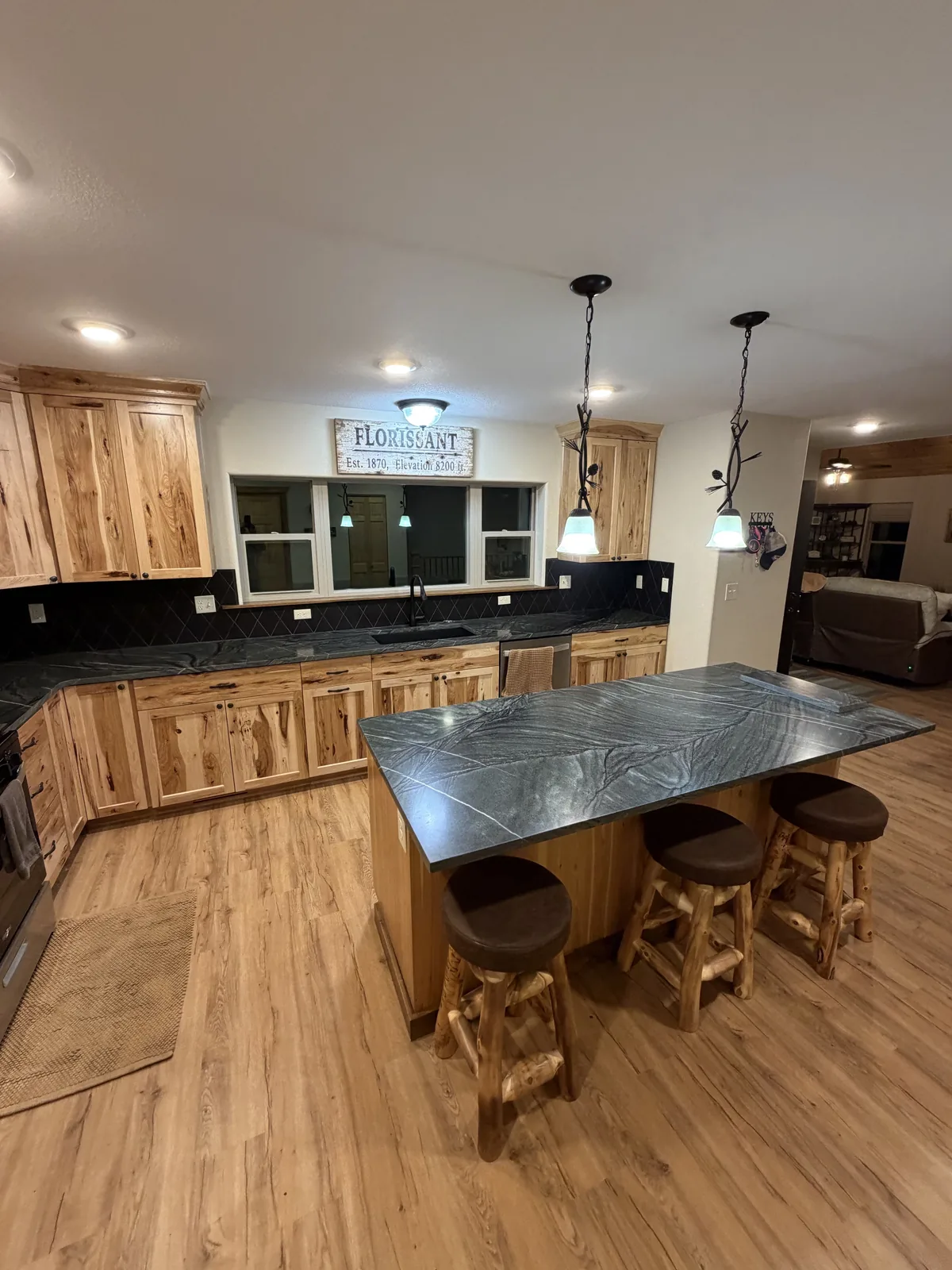 Second angle of a kitchen with dark stone island and wood cabinets